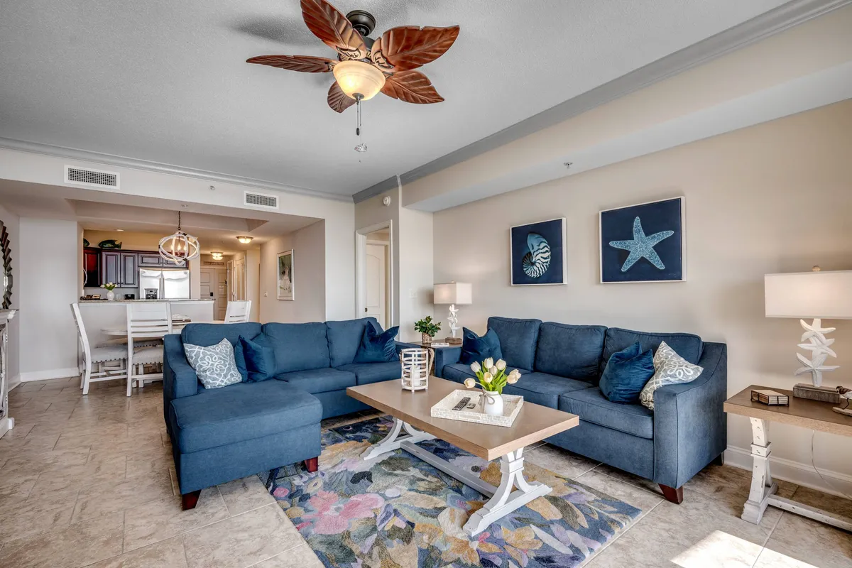 A comfortable living room with a coordinated sofa set and coffee table, accented by elegant wall art and a ceiling fan. The space is designed for both relaxation and socializing, providing an inviting atmosphere for movie nights or conversations.