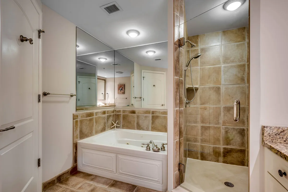 A luxurious bathroom scene featuring a large bathtub, spacious shower area, mirrors, and a granite countertop. The space feels tranquil and pristine, ideal for unwinding in privacy after a busy day.