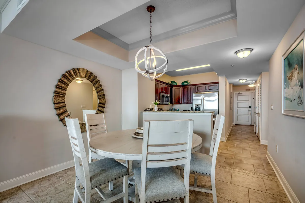 An inviting dining area featuring a stylish dining table under a chandelier, with a large mirror that reflects the adjacent kitchen and living space. The open layout allows for easy movement and conversation, setting the scene for family meals or game nights.