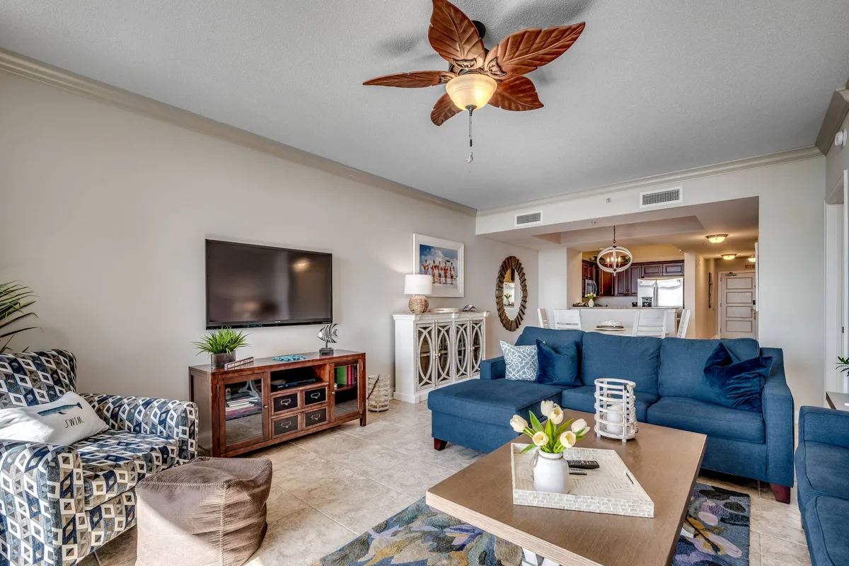 A stylish living area with a deep blue couch, decorative ceiling fan, and a coffee table topped with a vase. The space is bright and inviting, designed for both relaxation and socializing, with the sofa bed offering extra sleeping flexibility for guests.