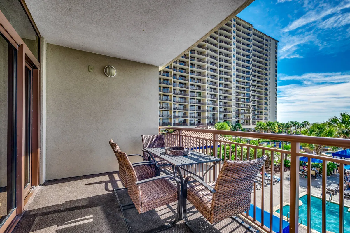 A sunny balcony furnished for outdoor dining, overlooking the pool and landscaped grounds. The setup invites guests to enjoy breakfast while taking in sunrise views and the fresh air, tying in the narrative’s mention of dining al fresco.